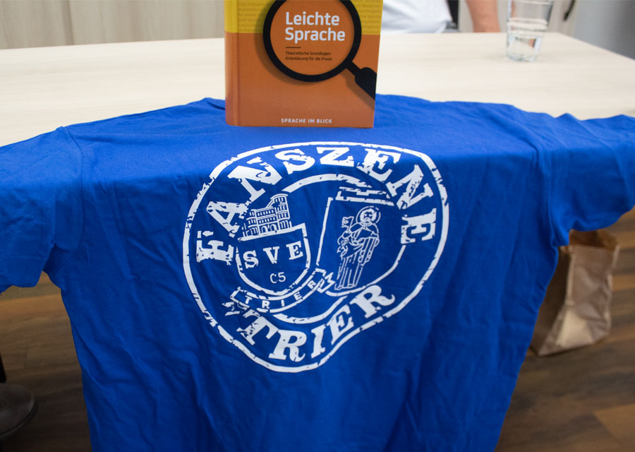 Ein T-Shirt der Fanszene Trier hängt als Kulisse für das Gespräch über einem Tisch
