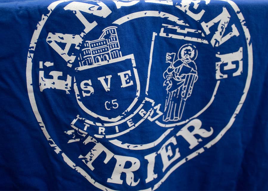 Das Logo der Fanszene Trier in weiß auf einem blauen T-Shirt