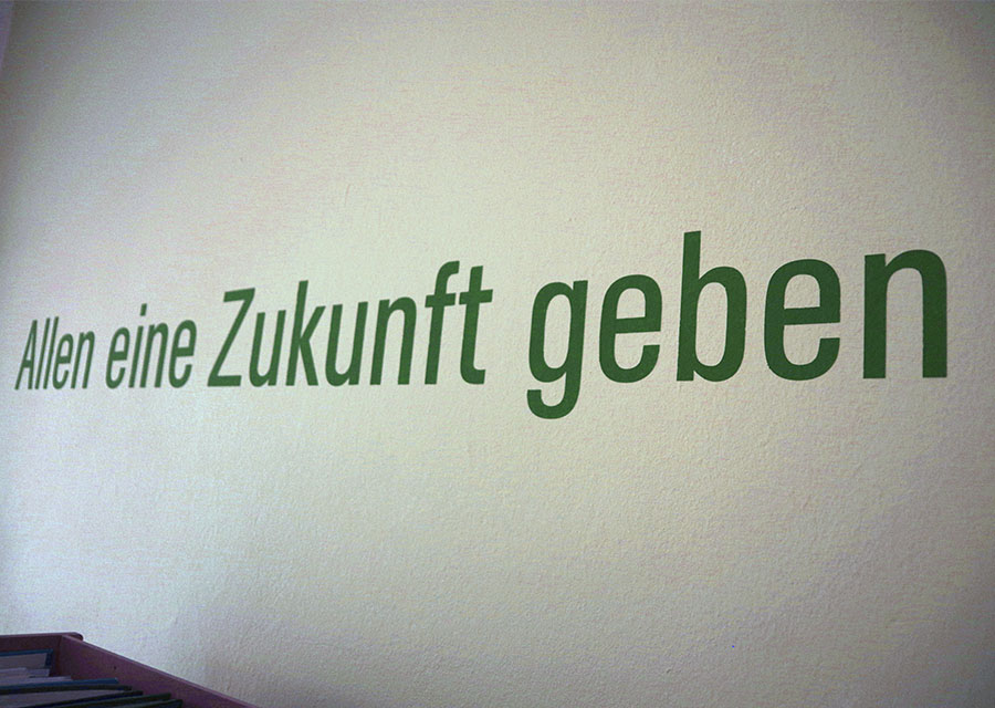 Schriftzug an der Wand, grün auf weiß: Allen eine Zukunft geben.