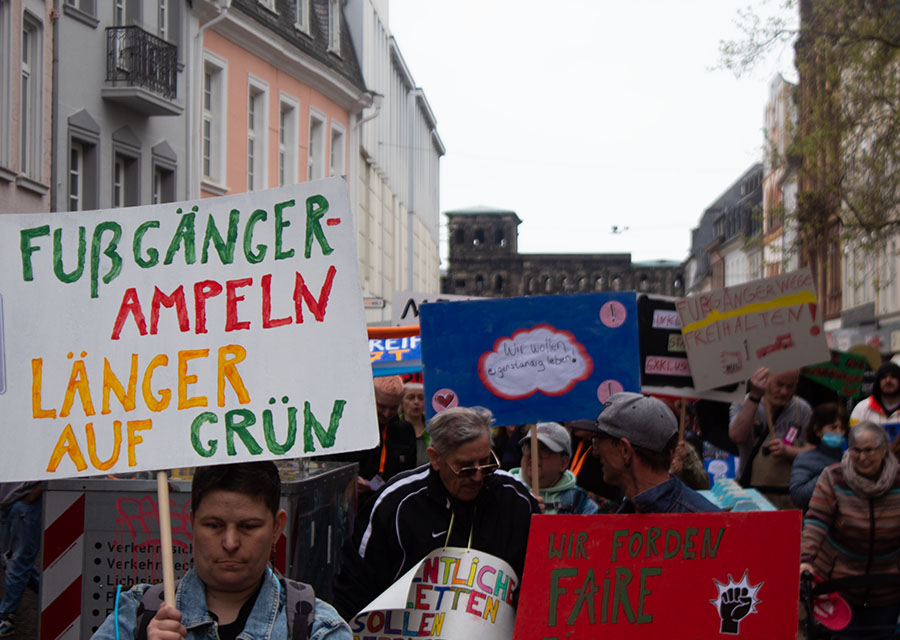 Menschen und viele Schilder beim Protestzug durch Trier, im Hintergrund die Porta Nigra