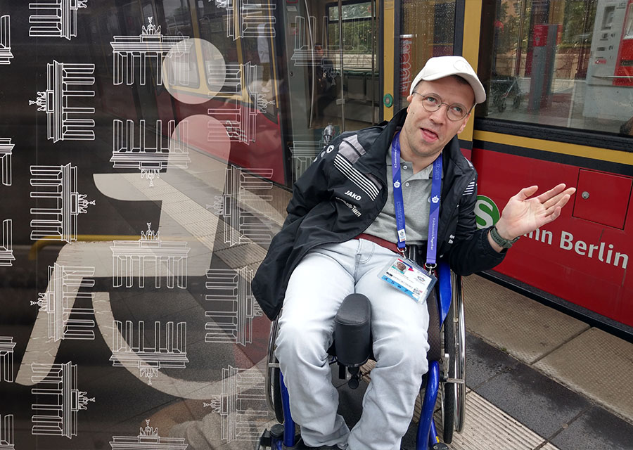 Patrick von TACHELES vor einer S-Bahn, links ins Bild das Rollstuhl-Zeichen eines S-Bahn-Fensters montiert