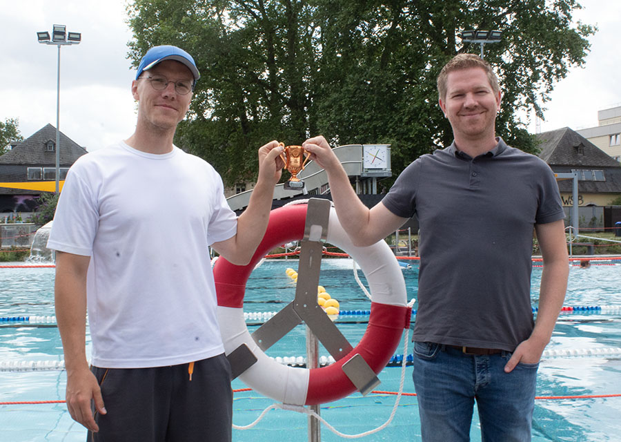 Ronny Engelbrecht und Bastian Junker präsentieren den Bronze-Pokal vor dem Schwimmbecken