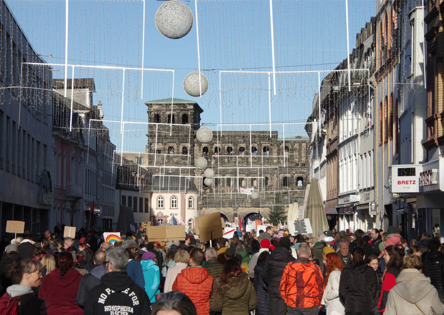 Blick von hinten auf eine große Masse an Menschen, die vor der Porta Nigra in Trier demonstriert