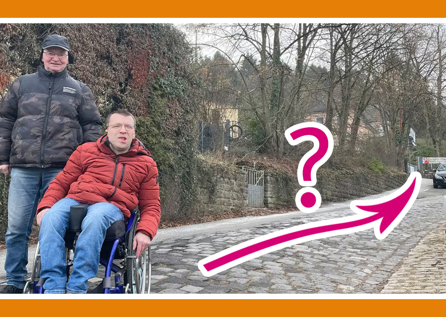 Michael (stehend) und Patrick (im Rollstuhl) von TACHELES stehen auf einer Straße mit Kopf-Stein-Pflaster, die bergauf geht. Dahinter Bäume und ein großes Gebäude, die Grundschule Kürenz, wo ein Wahlbüro ist. Im Bild ein magentafarbener Pfeil von ihnen den Berg hoch, darüber ein Fragezeichen. Beitragsbild