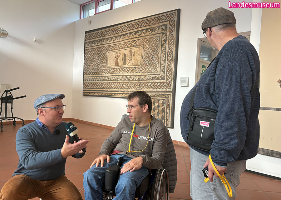 Marc vom SWR interviewt Patrick und Heinrich in einem Ausstellungsraum