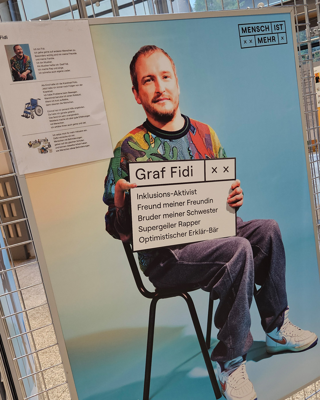 Bild aus der Ausstellung von Künstler und Rapper Graf Fidi mit seinem Foto und einer Tafel mit seinem Namen und Text in der Hand