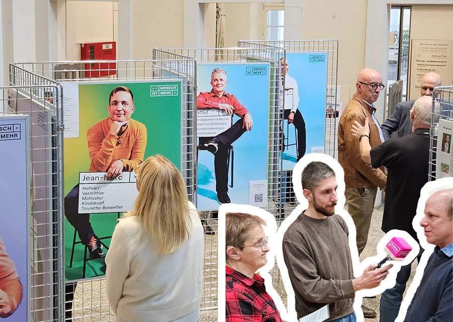 Blick von oben auf die Ausstellung: Foyer eines großen Hauses, helle Wände und Boden, Drahtaufsteller in Zickzackform aufgestellt, daran hängen Bilder von Leuten mit Beschriftung. Im Vordergrund: Martina Faßbender und Lucas Blasius interviewen Christian Ludwig, sie stehen sich gegenüber, Lucas hält ein magentafarbenes Mikrofon.
