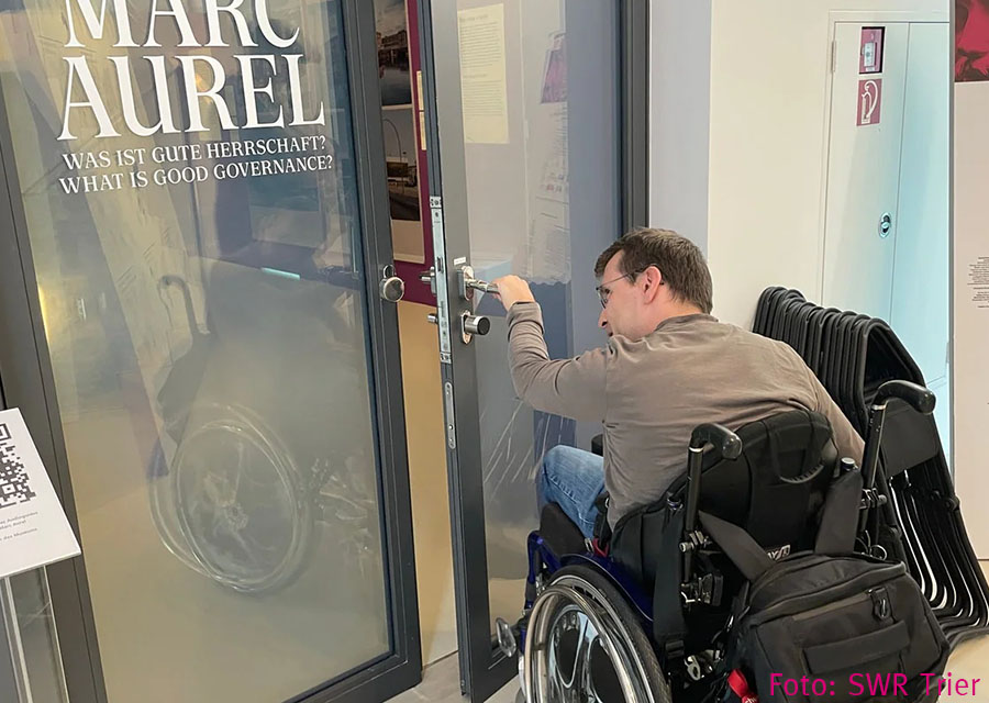 Patrick zieht an einer grauen Glastür mit der Beschriftung Marc Aurel