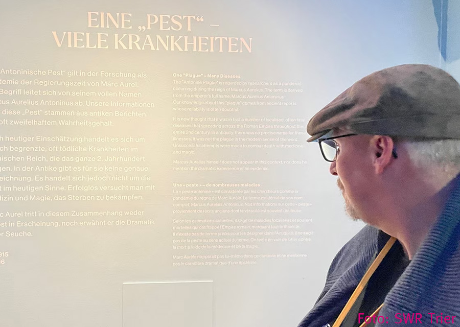 Heinrich schaut auf eine helle Wand mit heller Schrift, schwer zu lesen