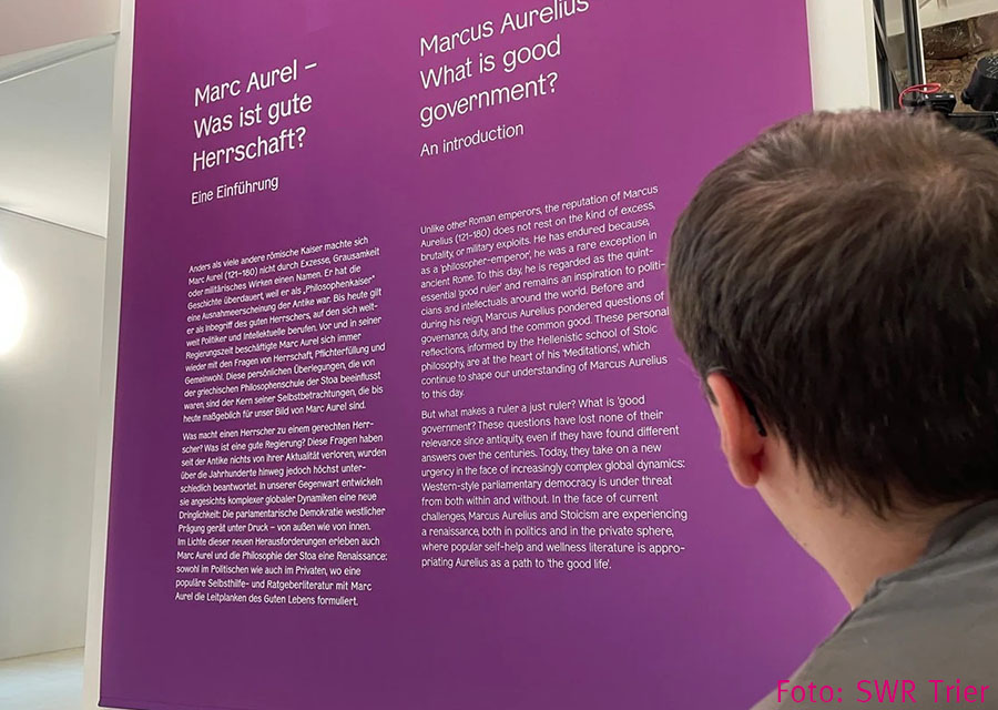 Patrick vor einer lilafarbenen Wand mit sehr viel kleinem Text