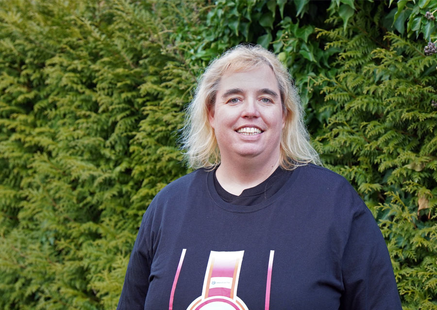 Redakteurin Monika im TACHELES-TShirt vor grüner Hecke